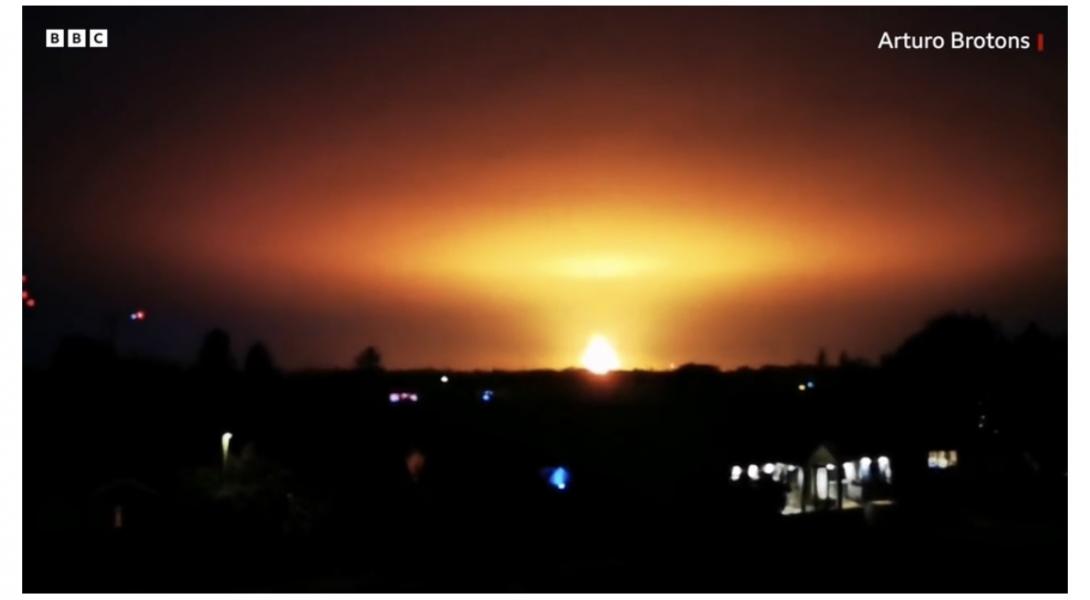 A massive explosion on the horizon, at nighttime
